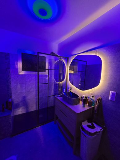 Salle de bains éclairée en bleu avec miroir, meuble-lavabo, lavabo et télévision murale éclairés