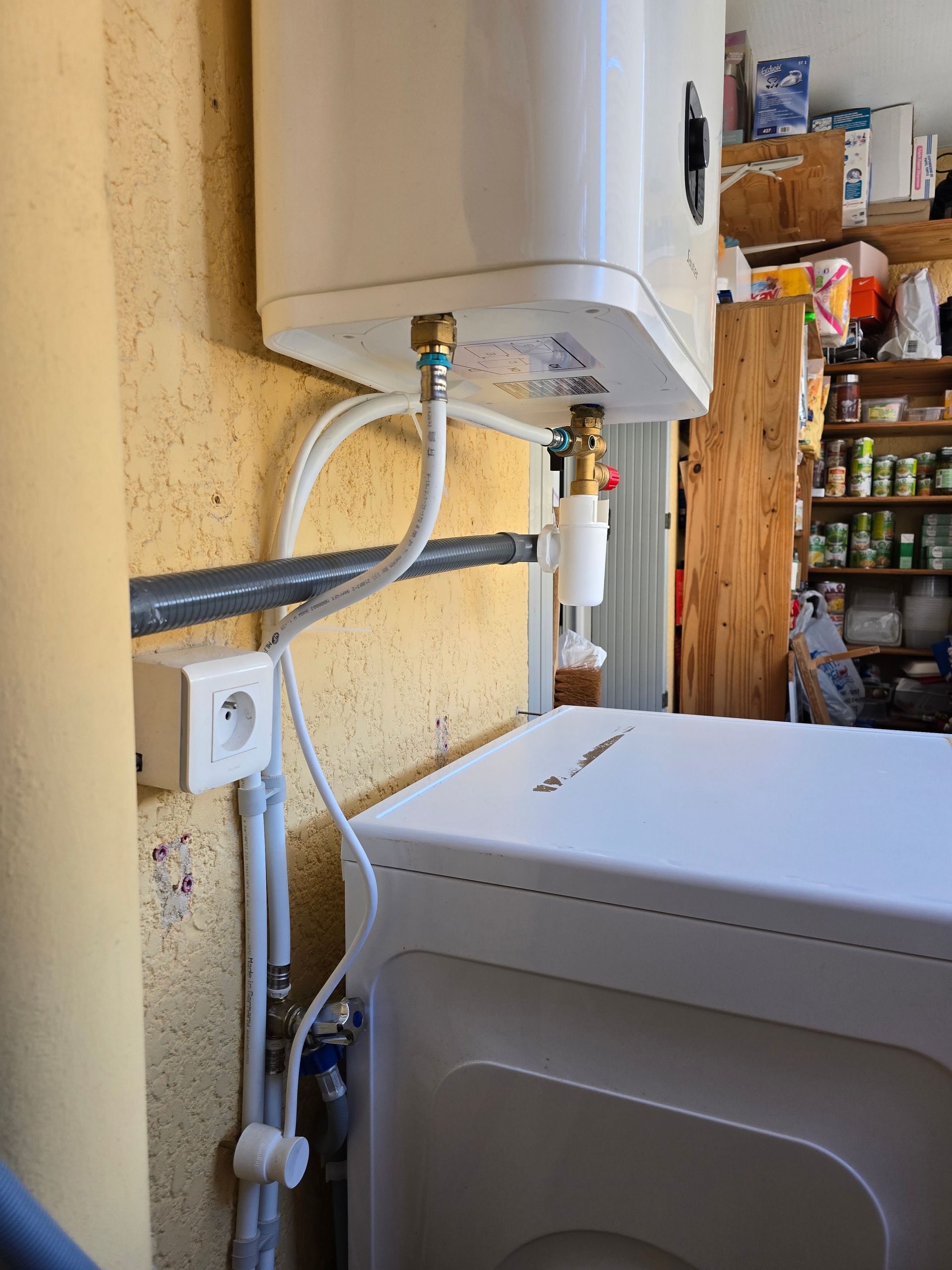 Buanderie avec chauffe-eau, tuyauterie, prise murale et lave-linge dans une pièce de service.