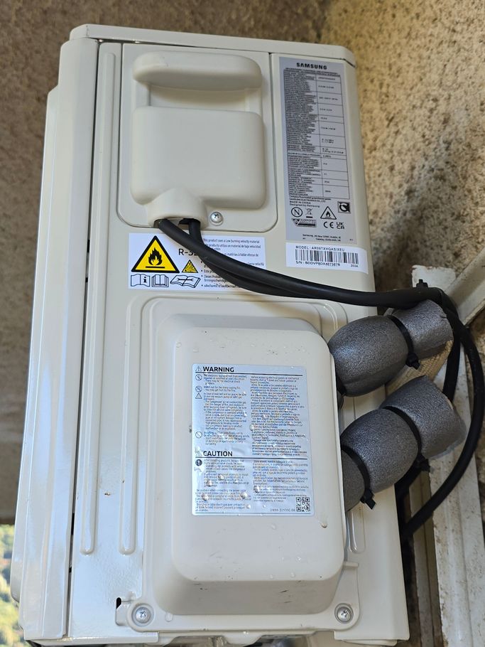 Dos d'un appareil électronique blanc avec étiquettes, câbles et isolation en mousse grise sur un sol moucheté