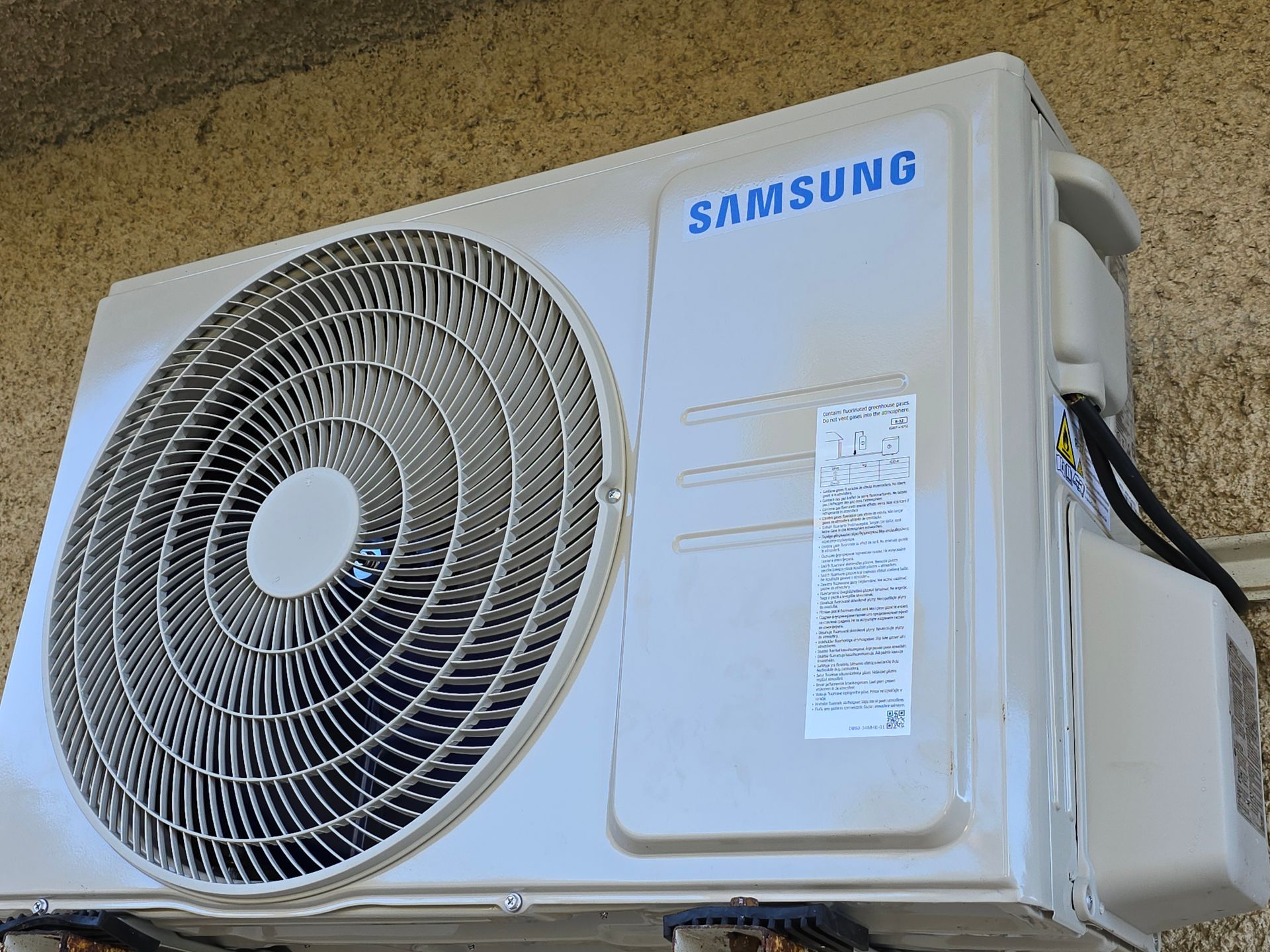 Unité de climatisation extérieure Samsung fixée au mur, boîtier blanc avec grande grille de ventilation.