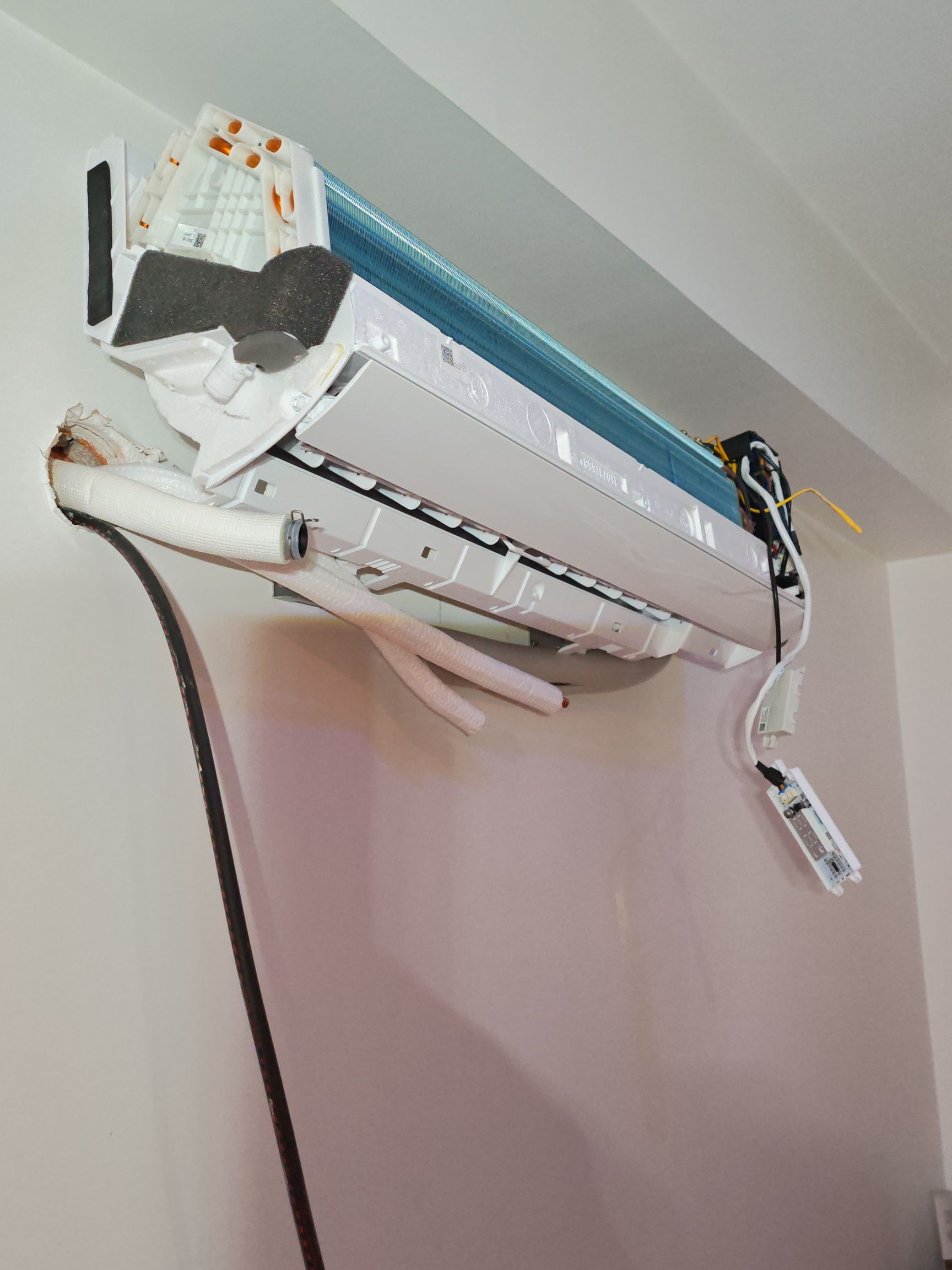 Climatiseur mural split dont le couvercle a été retiré, laissant apparaître les composants internes et les pièces pendantes.