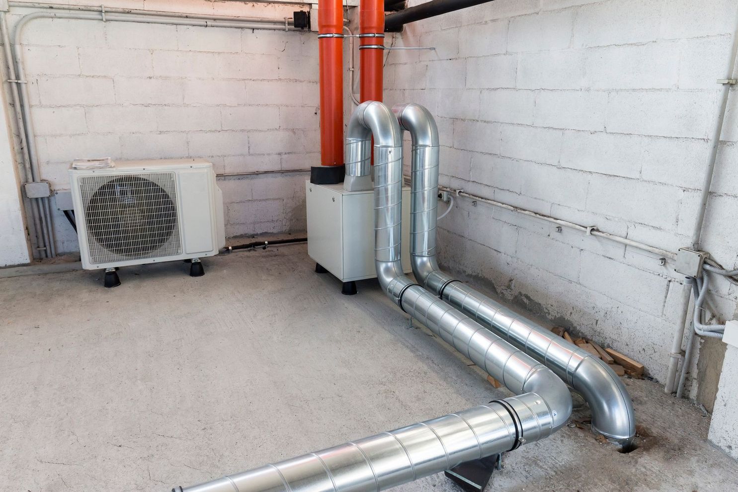 Tuyaux et unités de climatisation extérieurs situés à côté d'un mur du bâtiment, y compris une unité de climatisation blanche et des conduits argentés.