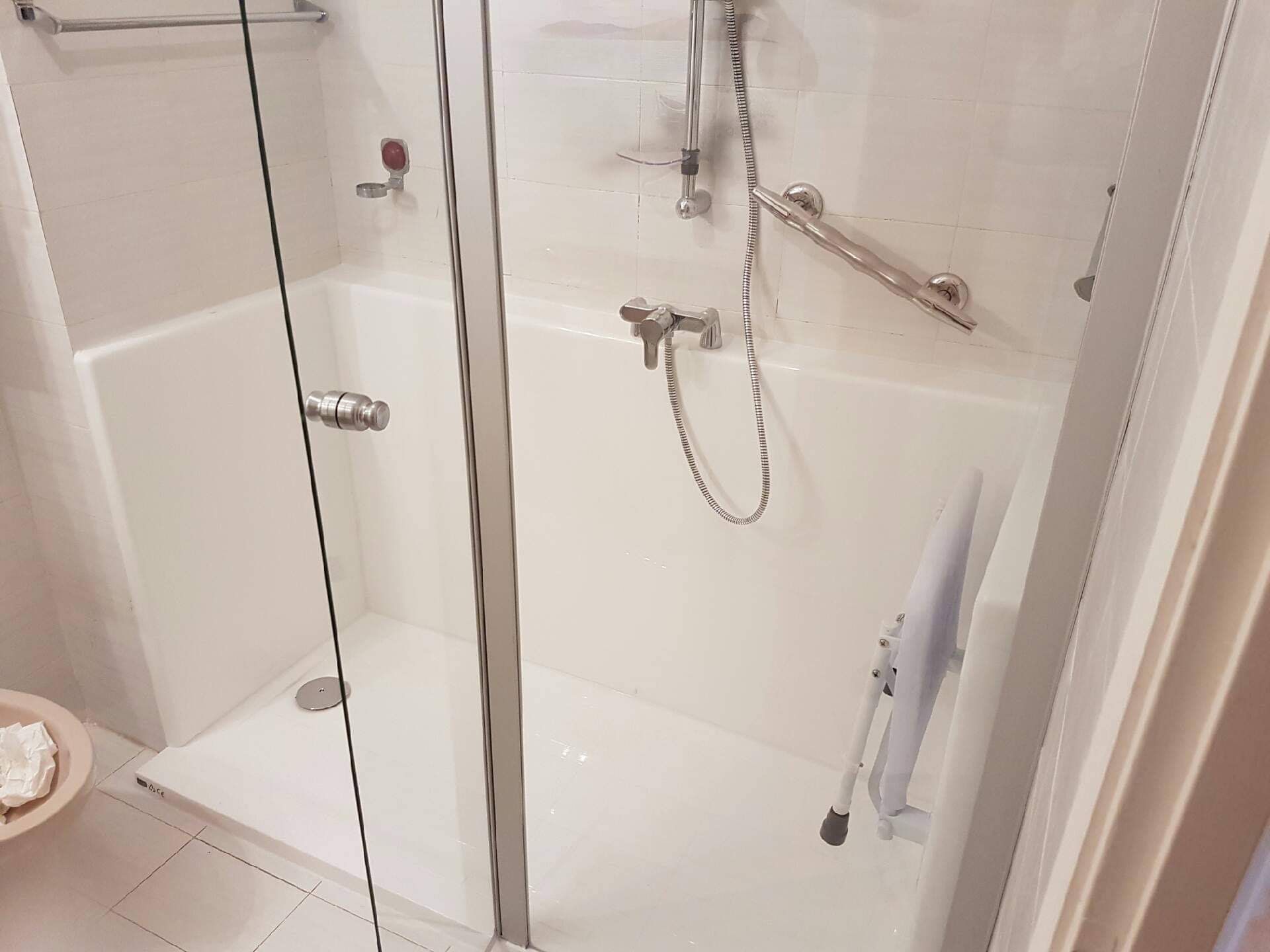 Cabine de douche blanche accessible avec barres d'appui, douchette et siège rabattable