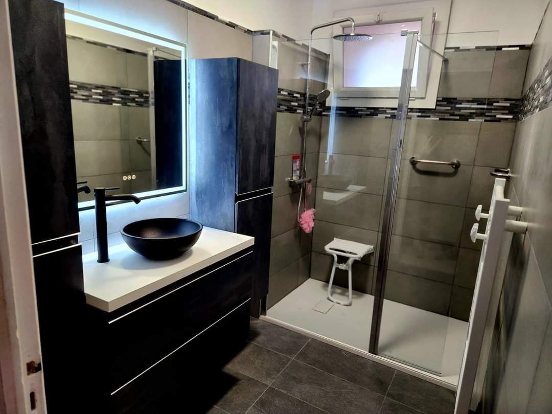 Salle de bains moderne avec douche à l'italienne, meuble-lavabo noir et vasque près d'une fenêtre
