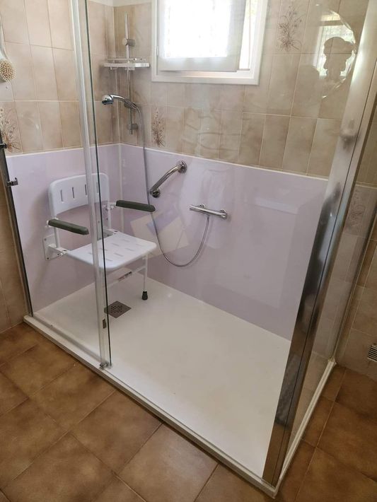 Douche à l'italienne avec porte en verre, siège rabattable et douchette dans une salle de bains carrelée beige