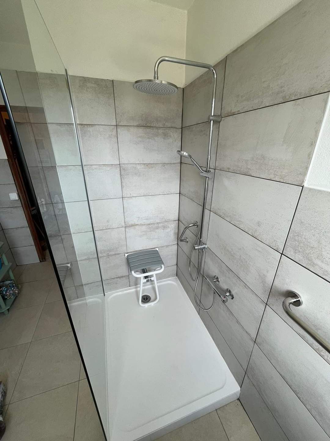Petite douche carrelée avec baignoire blanche, robinetterie chromée et pommeau de douche à main.