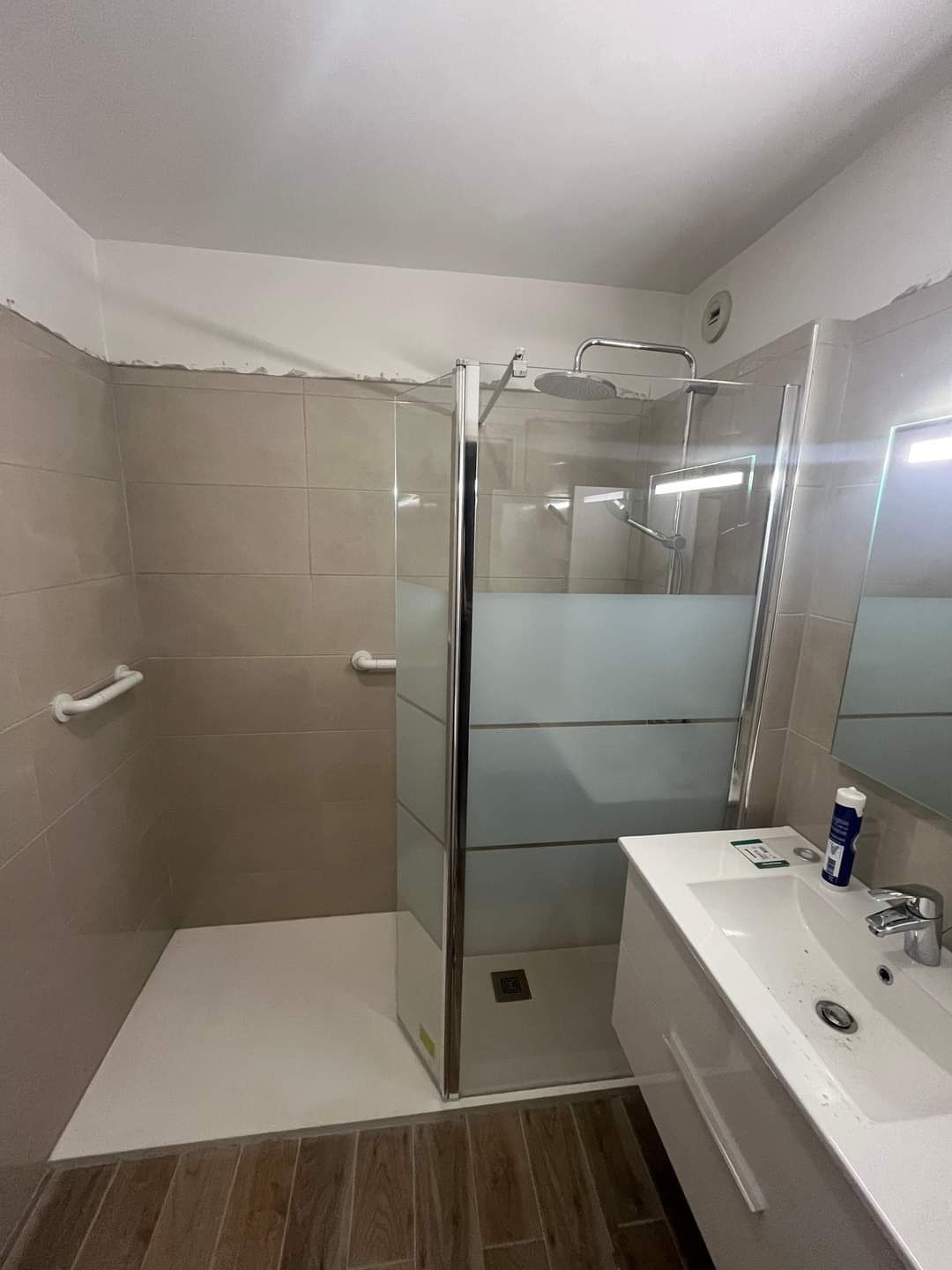 Petite salle de bains avec douche carrelée, porte en verre et meuble-lavabo blanc.