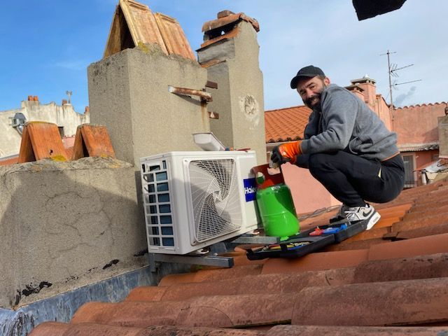 Un technicien répare un climatiseur de toit à côté de cheminées en briques et de tuiles en terre cuite.