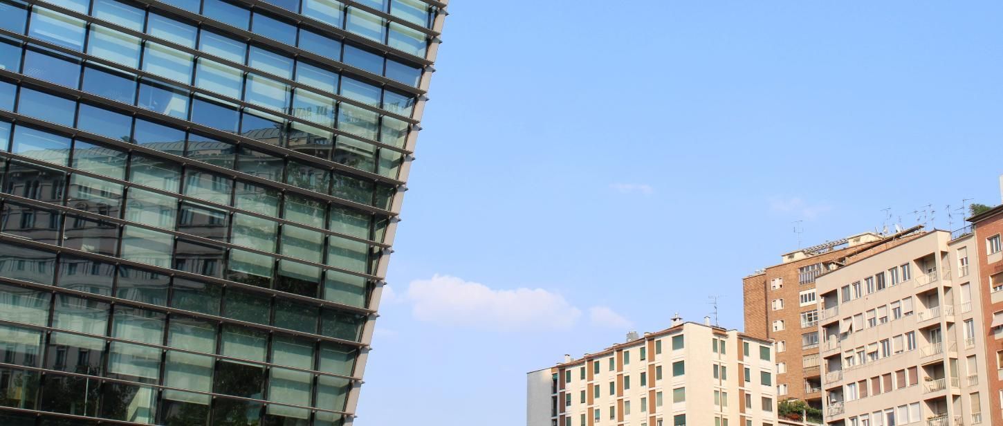 Edificio moderno de cristal junto a bloques de apartamentos beige bajo un cielo azul