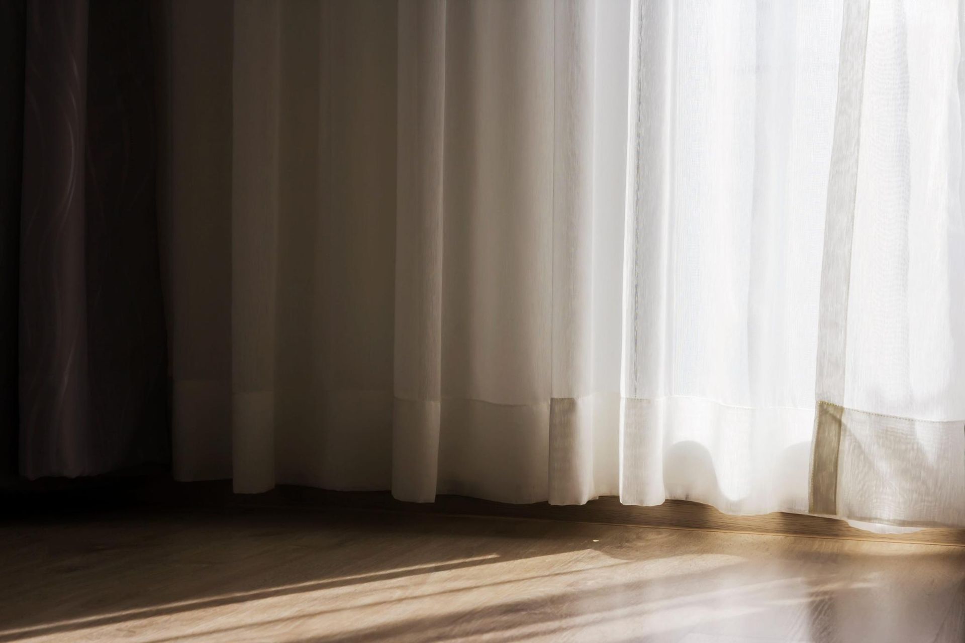 Cortinas transparentes que cuelgan sobre un suelo de madera bañado por el sol, con luz suave y sombras 