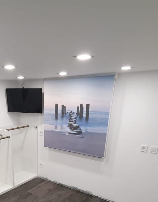 Habitación moderna de color blanco con luces empotradas, televisor montado en la pared y un gran cuadro con un paisaje 