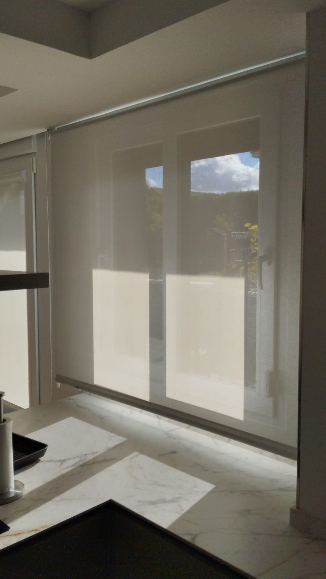 Habitación moderna con grandes persianas blancas y luz solar que proyecta sombras en el suelo.