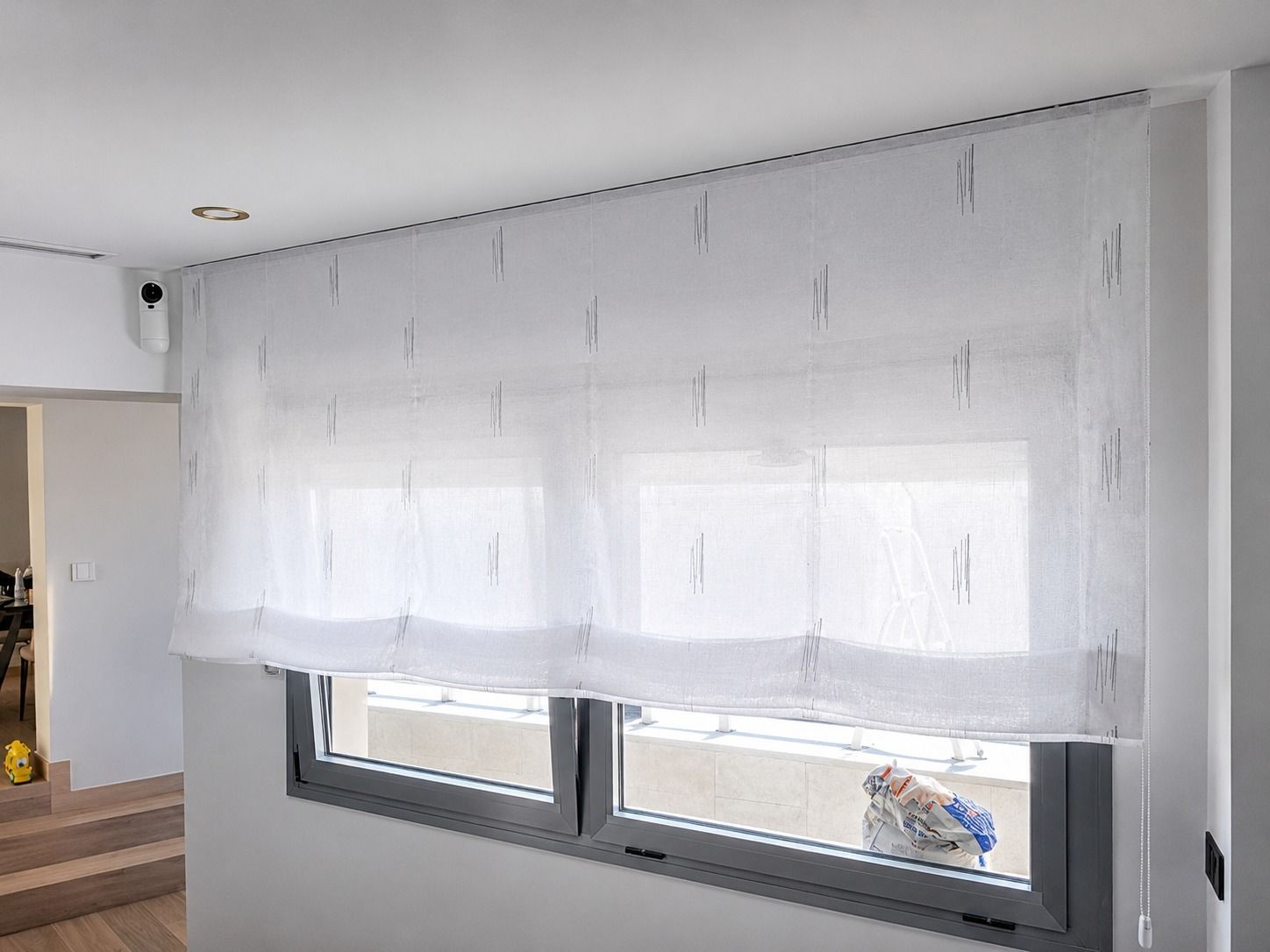 Estor romano blanco estampado sobre una pequeña ventana encima de un radiador blanco en una habitación azul claro.
