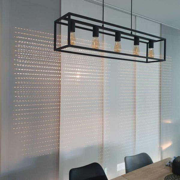 Sala de reuniones moderna con lámpara colgante negra, pared de cristal y sillas junto a una mesa de madera.