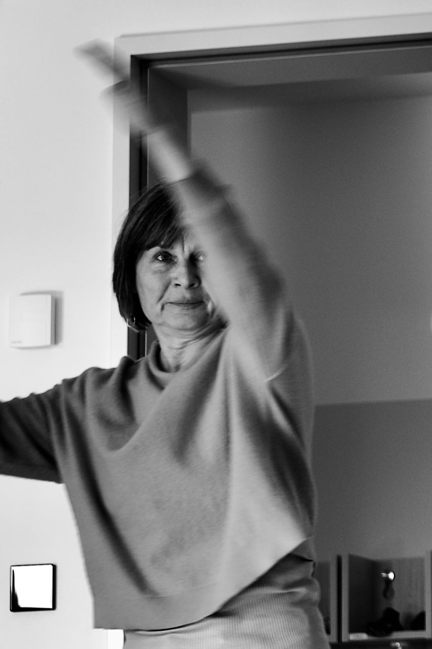 Person stretching with arms raised in a doorway, wearing a light sweater.