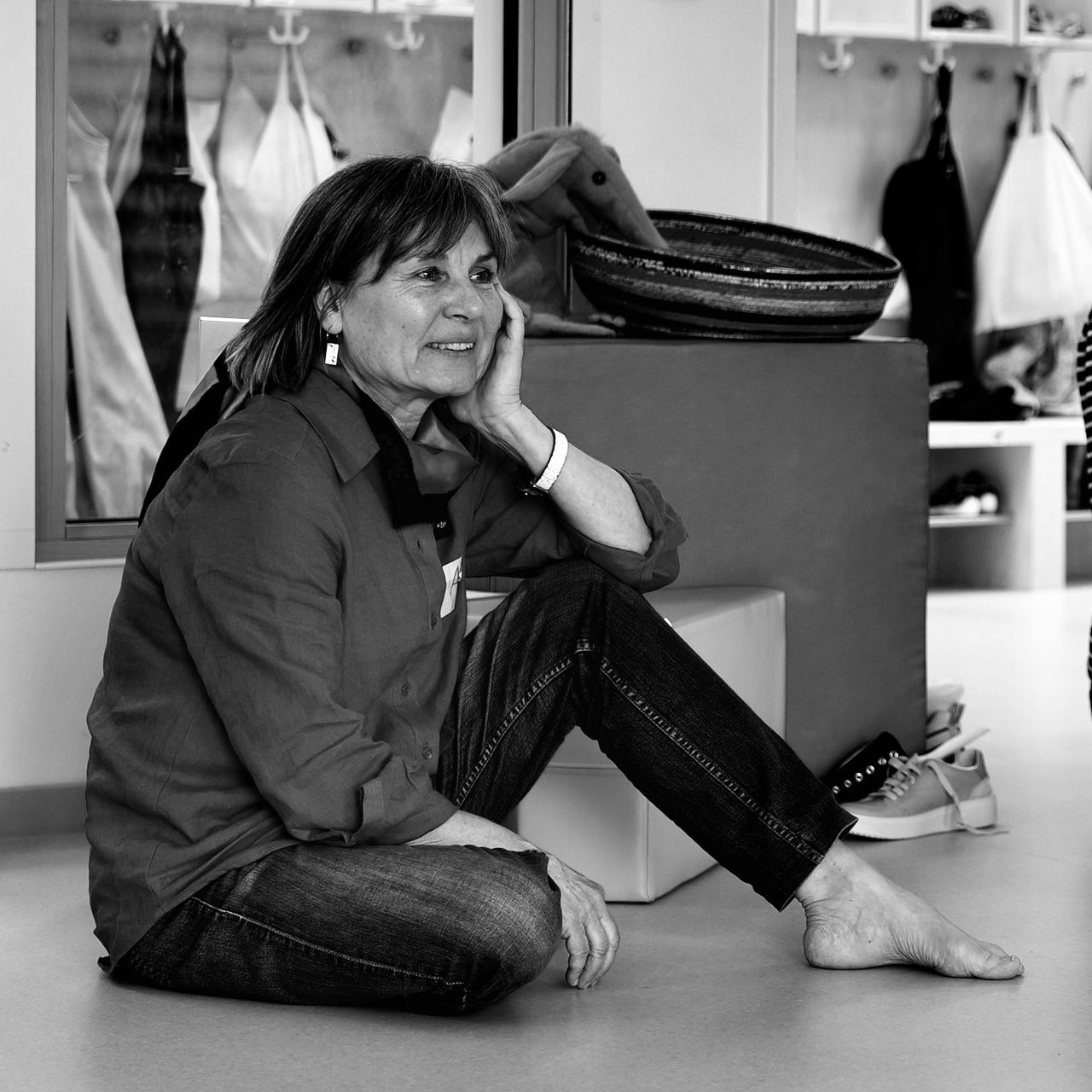 Woman sitting on the floor in a clothing store, resting her head on her hand beside a display table.