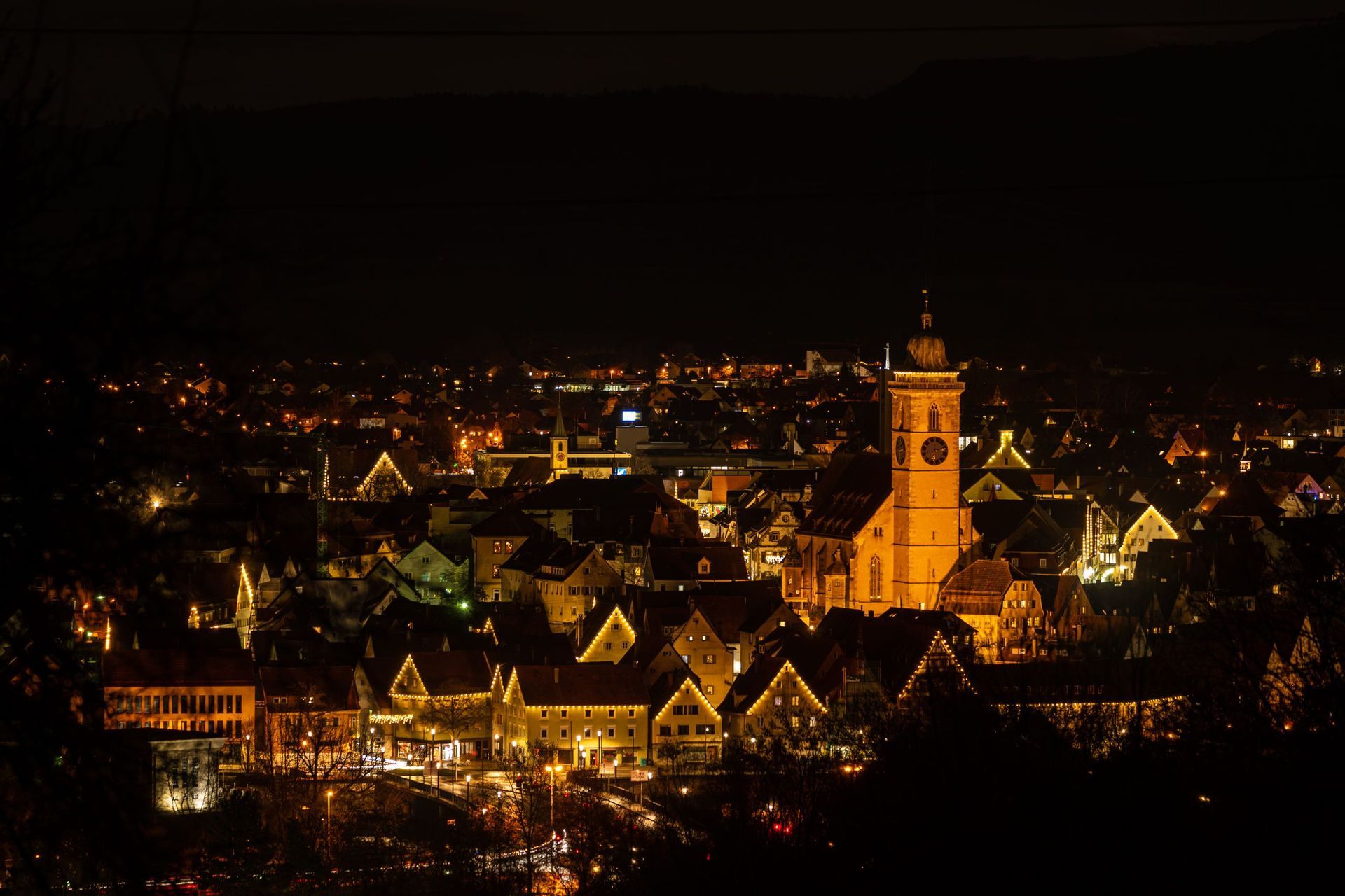 Nachtansicht einer deutschen Stadt, die mit goldenen Lichtern erleuchtet ist. Ein hoher Kirchturm dominiert die Skyline.