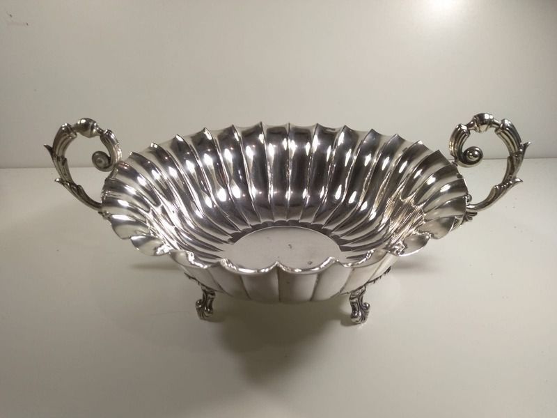 Un cuenco de plata con asas está sobre una mesa.