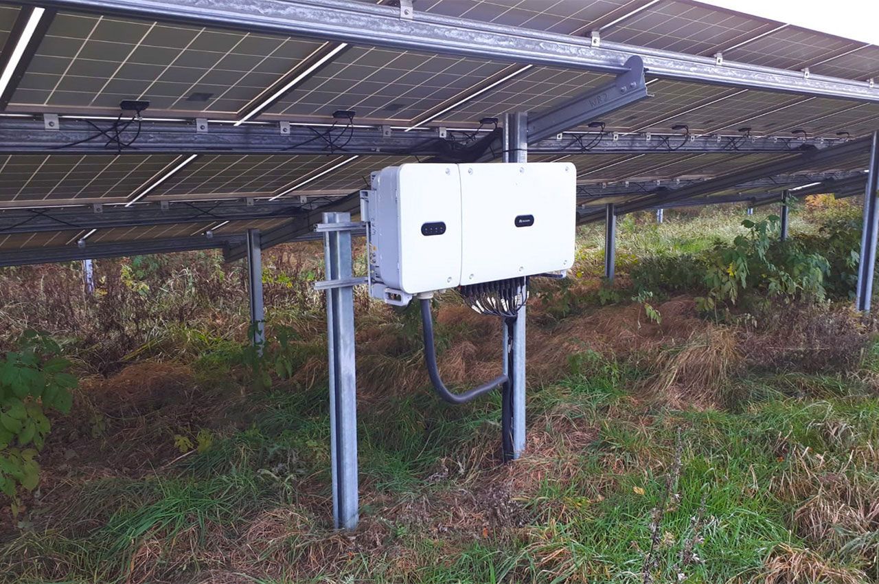 Auf einem Feld steht ein weißer Kasten unter einem Solarpanel.