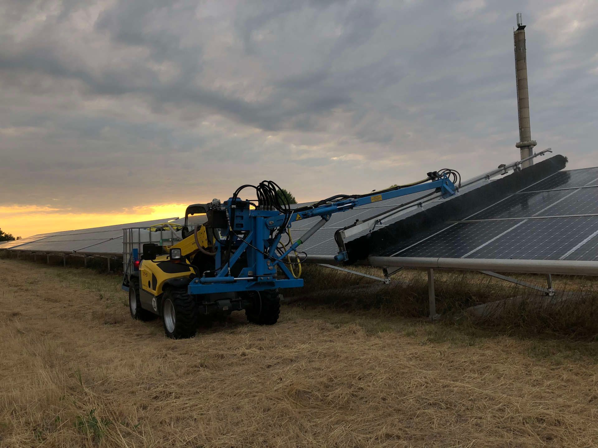 Ein blau-gelber Traktor reinigt Solarmodule auf einem Feld.