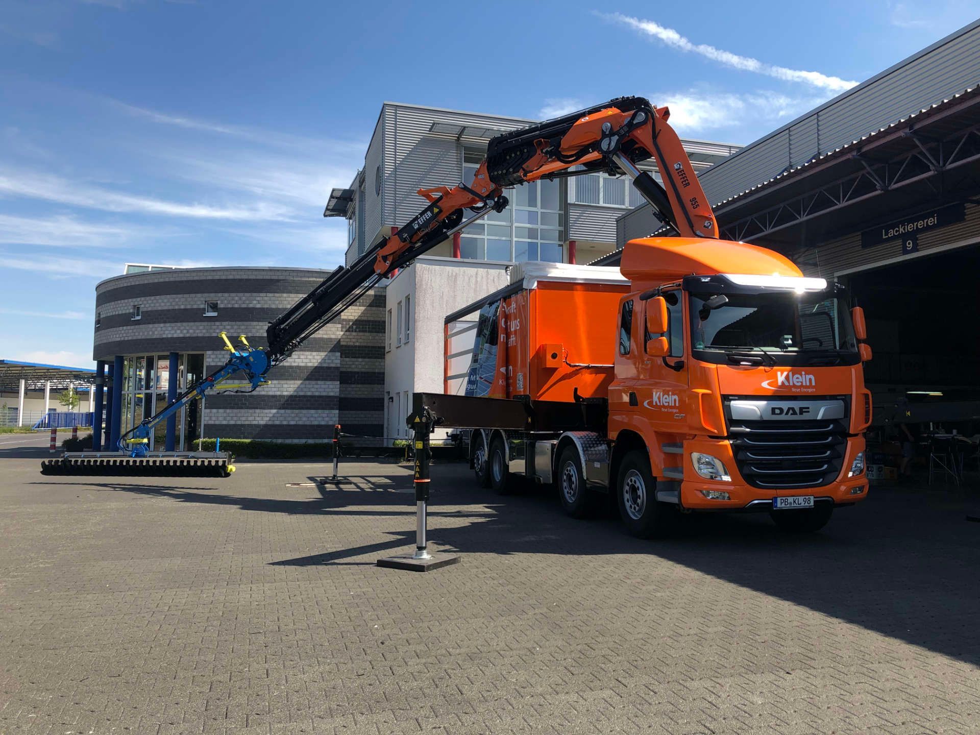 Ein orangefarbener Lastwagen mit einem daran befestigten Kran steht vor einem Gebäude.