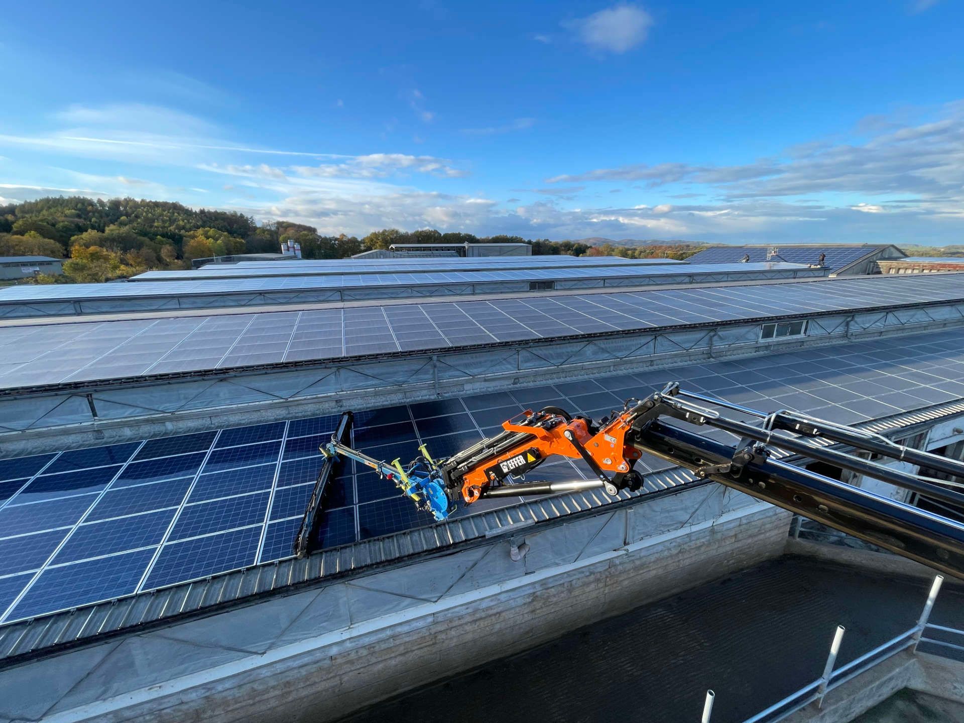 Ein Kran reinigt Solarmodule auf dem Dach eines Gebäudes.