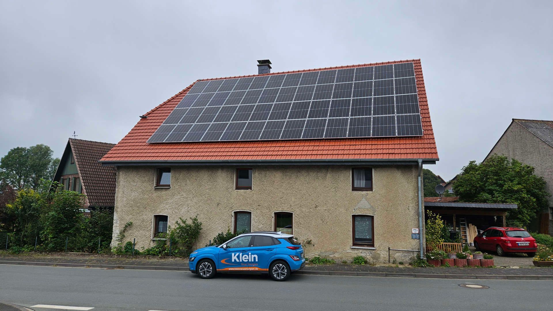 KNE Auto parkt vor einem Haus mit Solarzellen auf dem Dach.