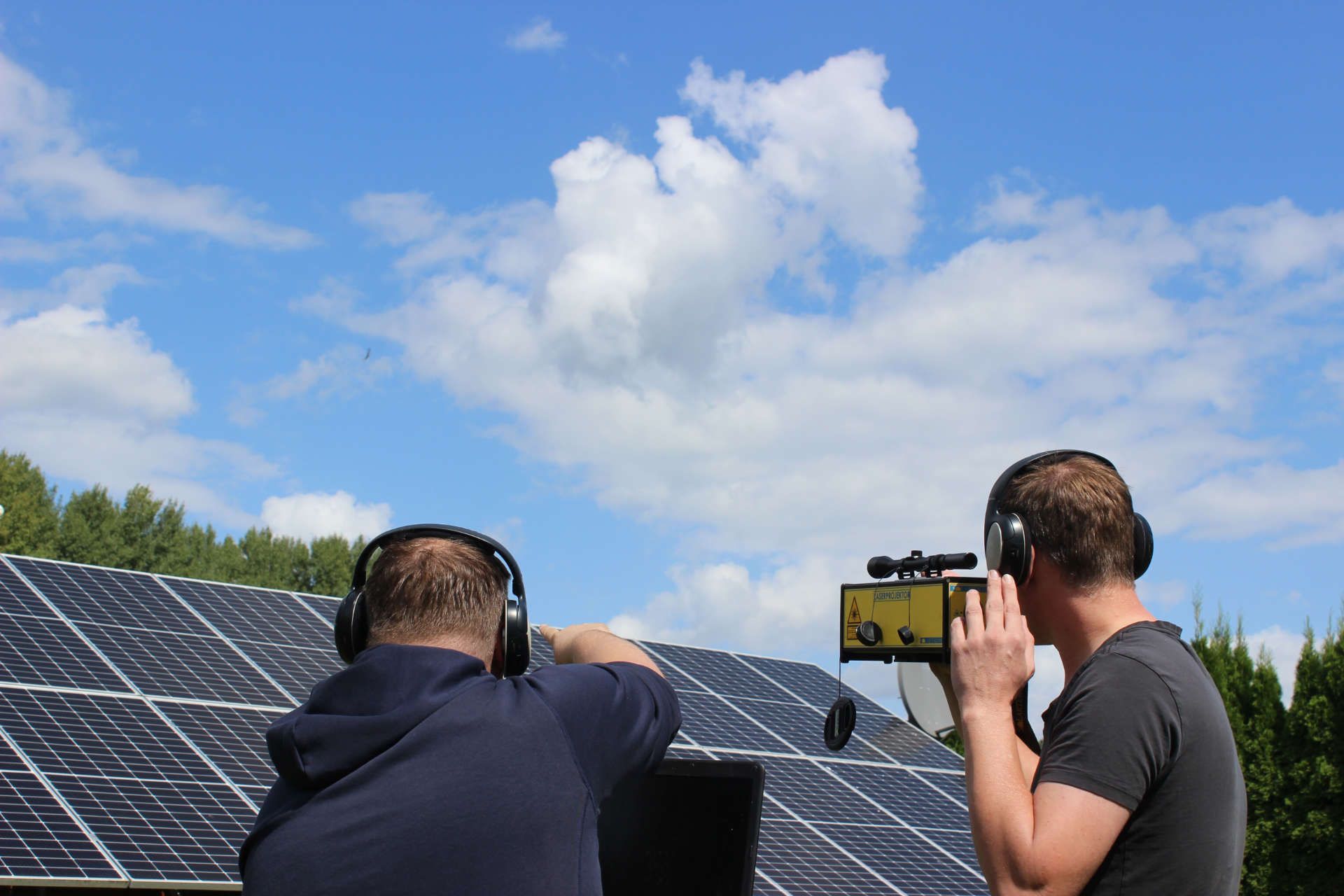 Zwei Männer mit Kopfhörern stehen vor einer Reihe von Solarmodulen