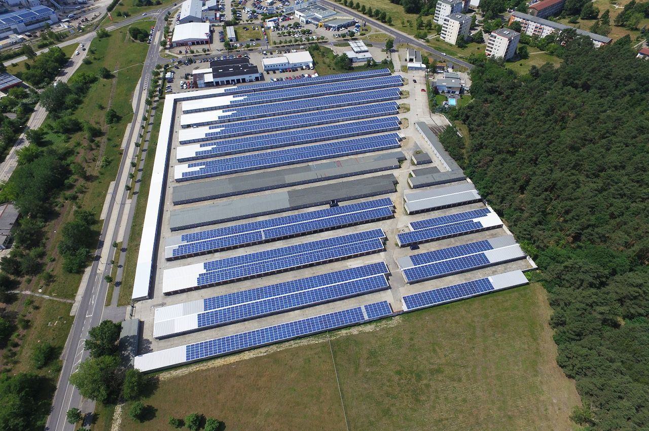 Eine Luftaufnahme einer großen Lagerhalle mit vielen blauen Solarmodulen auf dem Dach.