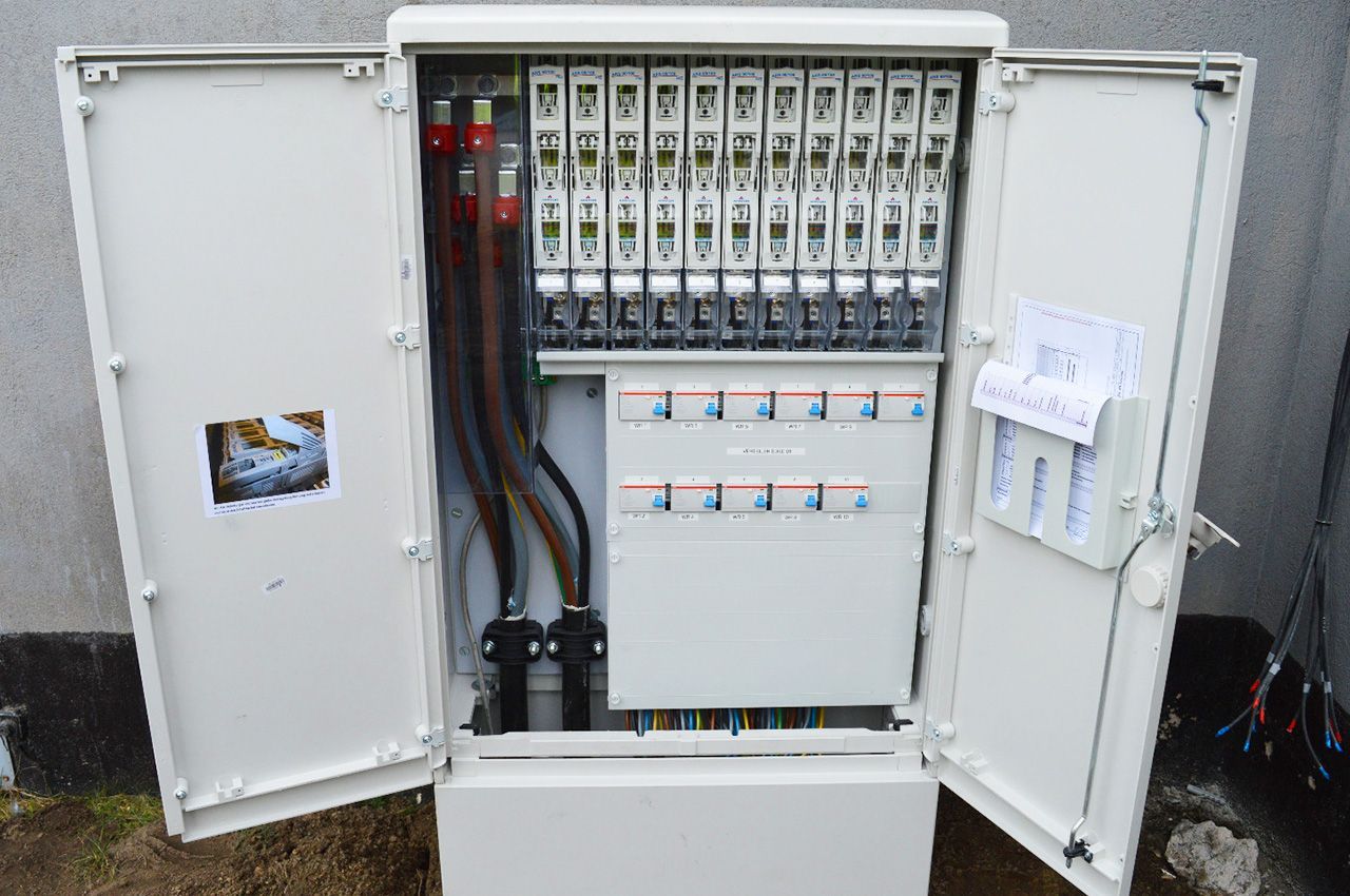 Ein weißer Sicherungskasten mit geöffneten Türen steht im Dreck.