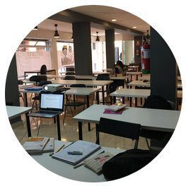 Un aula con mesas y sillas y una computadora portátil en un escritorio.