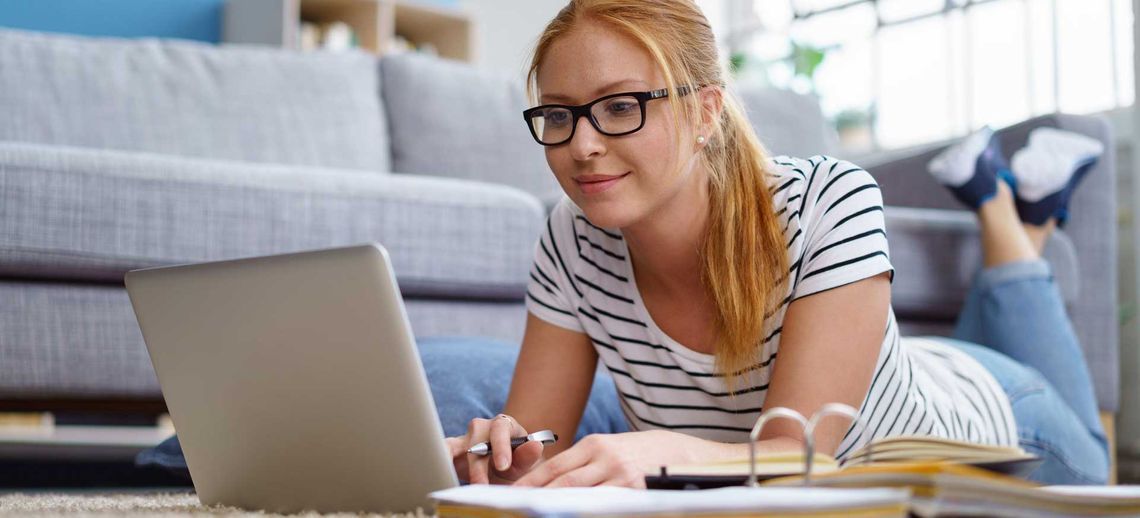 Una mujer está tumbada en el suelo utilizando una computadora portátil.