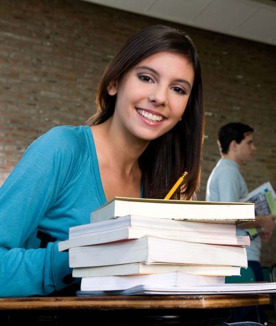 Una mujer se sienta en un escritorio con una pila de libros y un lápiz.