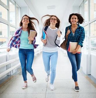 Tres mujeres jóvenes caminan por un pasillo sosteniendo libros.