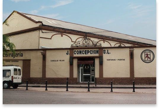 Una camioneta blanca está estacionada frente a un edificio que dice jj concepcion sl