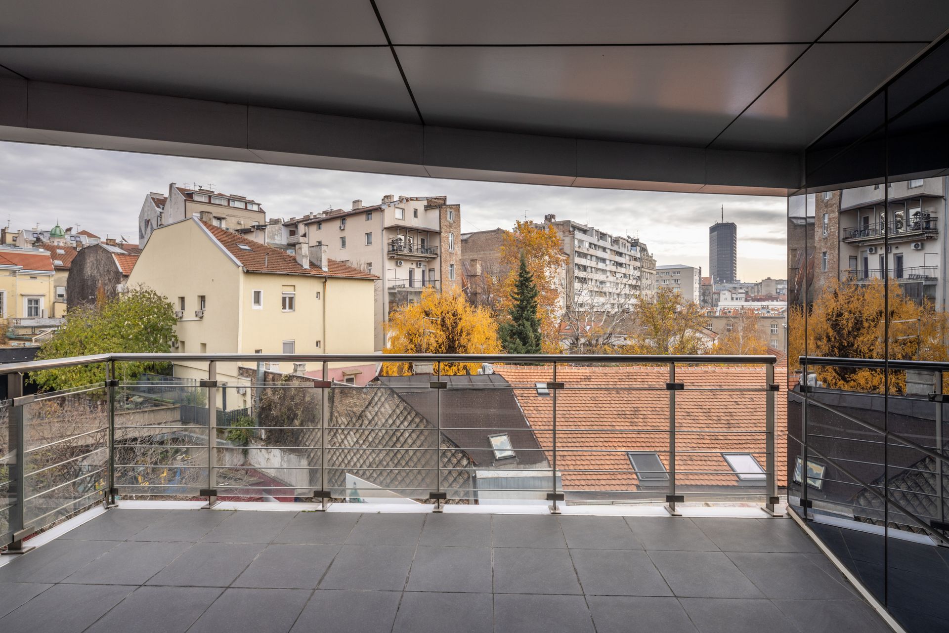 Balcon donnant sur un paysage urbain composé d'immeubles aux balustrades en verre et sous un ciel nuageux.