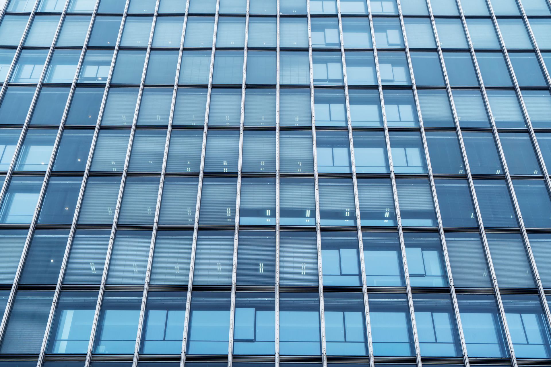 Façade en verre bleu et métal d'un immeuble de bureaux moderne, avec stores.