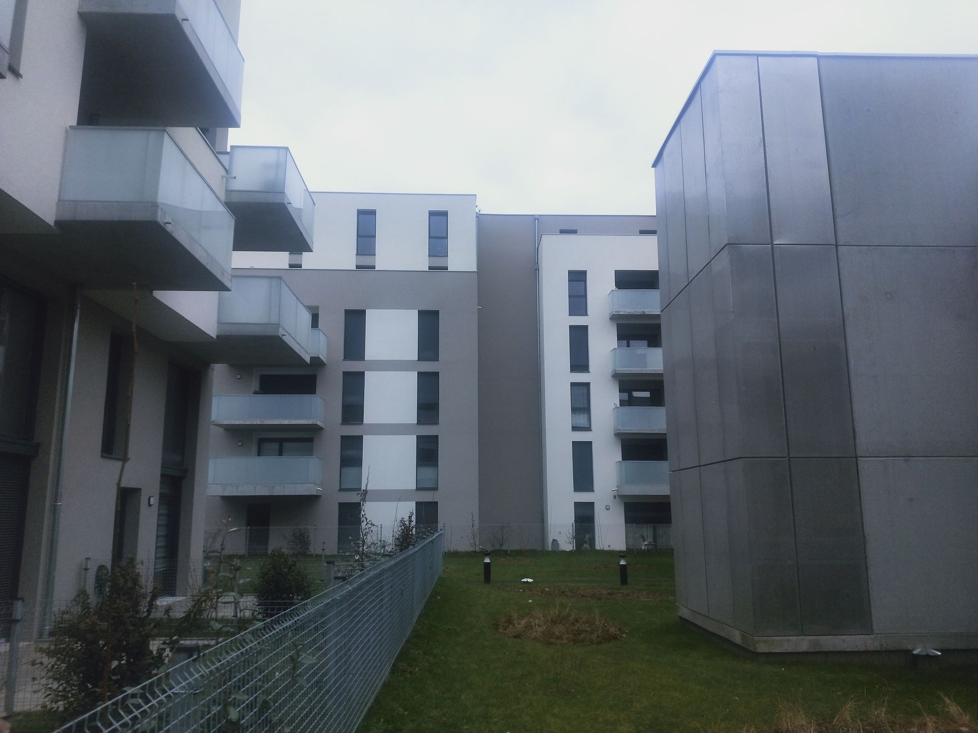 Balcon donnant sur un paysage urbain composé d'immeubles aux balustrades en verre et sous un ciel nuageux.