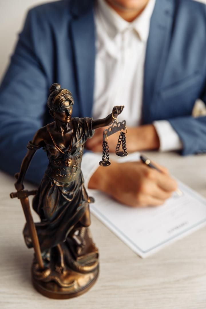 Una estatua de la justicia está sentada en una mesa junto a un hombre que firma un documento.