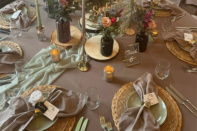Ein für einen Hochzeitsempfang gedeckter Tisch mit Tellern, Servietten, Kerzen und einer Tischnummer.