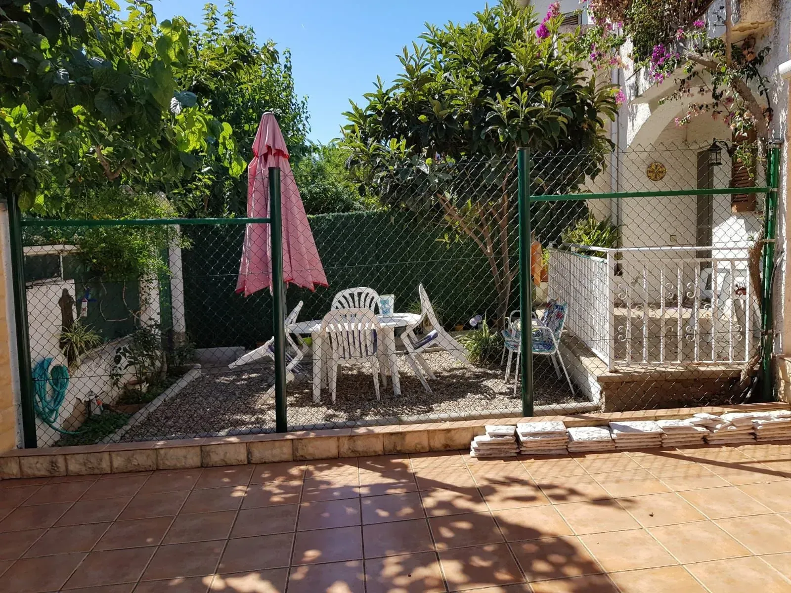 Un patio con una mesa y sillas y una sombrilla rosa detrás de una cerca de alambre.