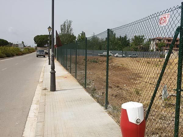 Un bote de basura rojo y blanco se encuentra junto a una cerca de alambre.