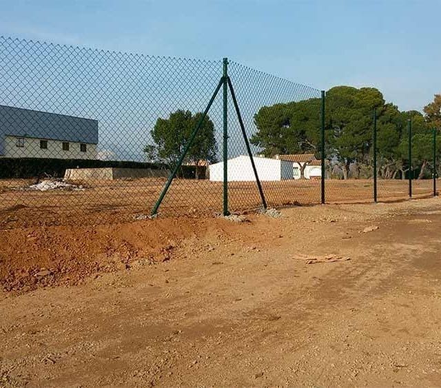 Una valla de alambre rodea un campo de tierra.