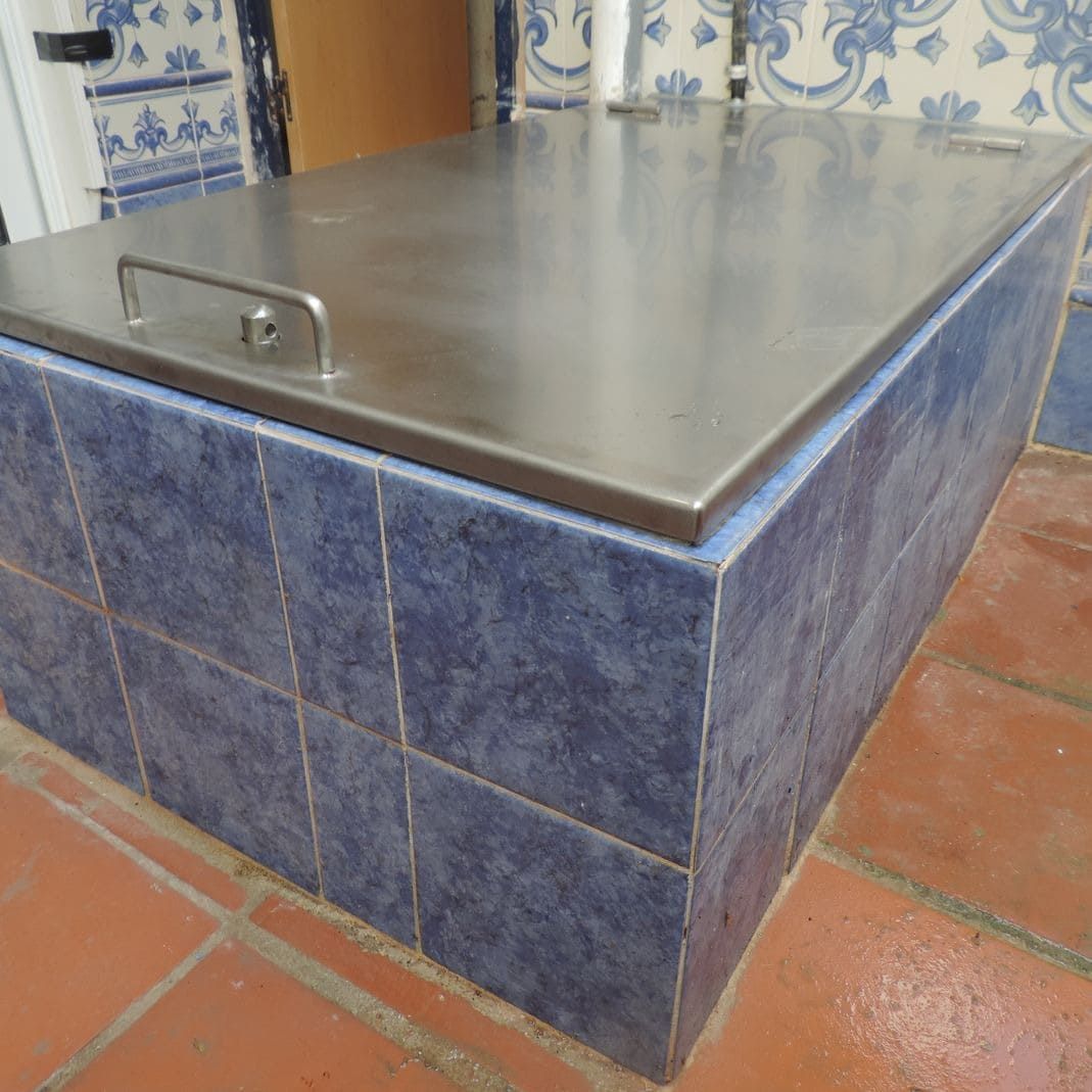 Una tapa de acero inoxidable reposa sobre un suelo de baldosas azules y blancas.