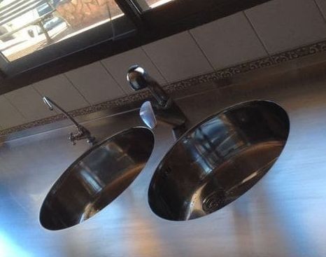 Dos fregaderos de acero inoxidable sobre una encimera con una ventana al fondo.