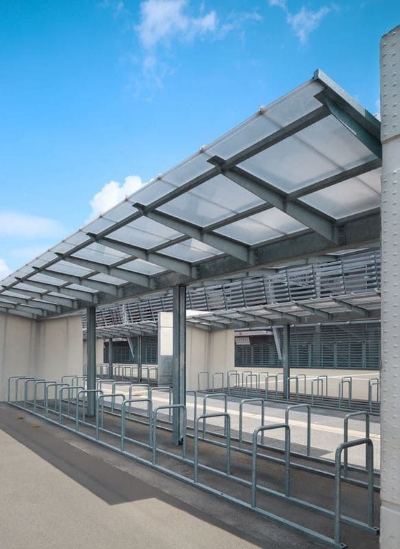 Una fila de portabicicletas bajo un dosel con un cielo azul de fondo