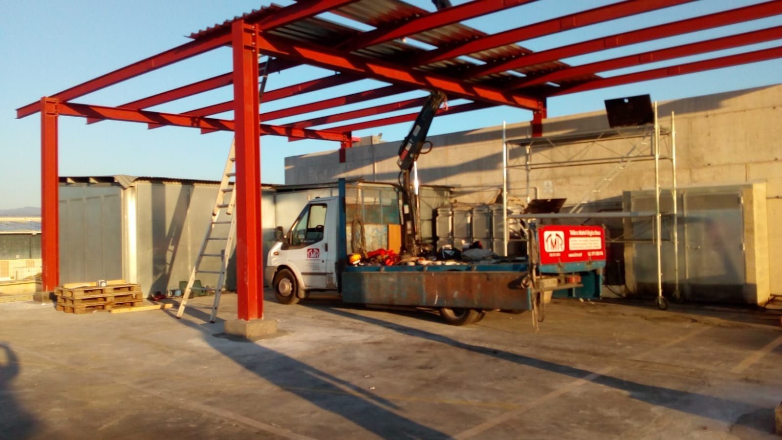 Una camioneta blanca está estacionada debajo de una estructura metálica roja.
