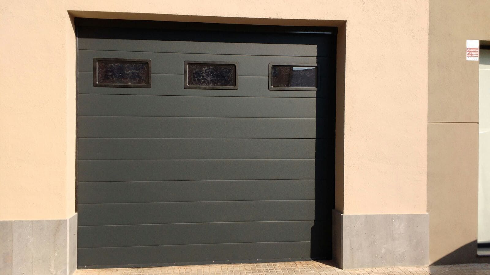 Una puerta de garaje negra está colocada al costado de un edificio.