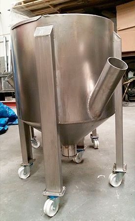 Un gran tanque de acero inoxidable con ruedas está sentado en el suelo en un almacén.