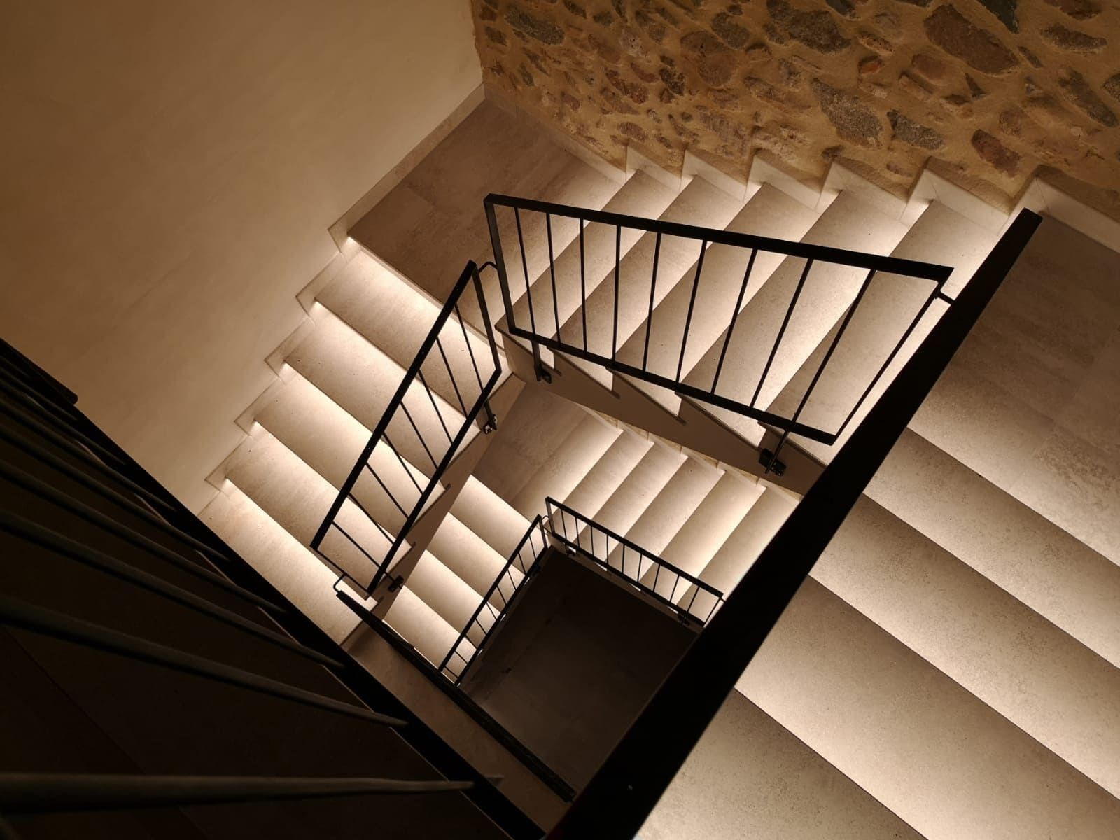 Una escalera con luces en los escalones y una barandilla de metal.